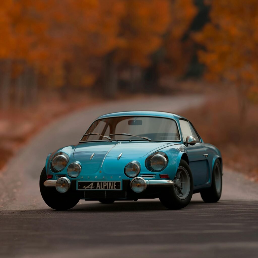 Classic Alpine A110 sports car driving on an autumn road with vibrant foliage.